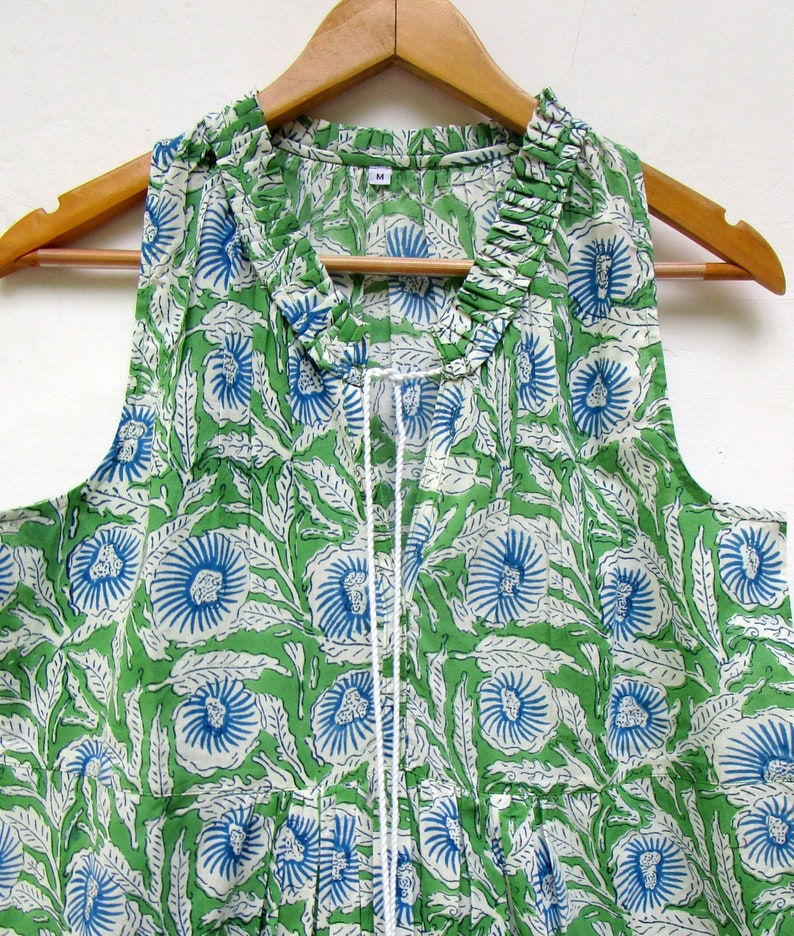 May include: A sleeveless green cotton top with a white and blue floral print. The top has a ruffled neckline and a drawstring closure.