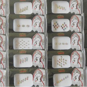 May include: A set of 12 packs of assorted rhinestones and jewels for applying to the forehead or face. Each pack contains a variety of shapes and sizes of rhinestones in different colours, including clear, white, silver, gold, blue, green, red, and pink.