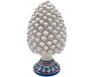 Puede incluir: Escultura de piña de pino de cerámica blanca con una base de patrón azul y blanco.
