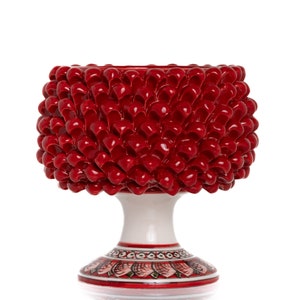 Peut inclure: Un pot en céramique rouge en forme de pomme de pin avec une base blanche et un motif peint. Le pot est une pièce décorative pour les plantes d'intérieur.