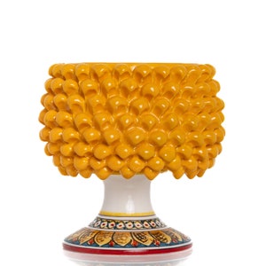 Può includere: Un vaso in ceramica giallo a forma di pigna con una base bianca e dettagli dipinti colorati. Il vaso ha un'ampia apertura rotonda e una base stretta.