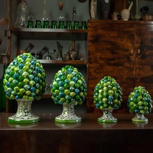 Può includere: Quattro alberi di pino in ceramica di diverse dimensioni, con dettagli dipinti in verde e blu. Gli alberi sono su una superficie di legno.