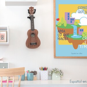 May include: A brown ukulele hanging on a white wall, next to a framed print with the text "CONOCE LO QUE VALES, AMA LO QUE HACES, CREE EN TI MISMO" in Spanish. The print features a colorful illustration of a floating island with buildings and a hot air balloon.