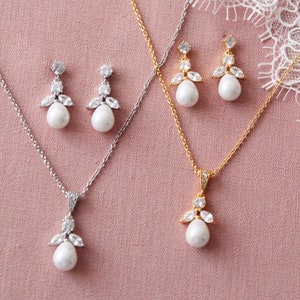 May include: Two sets of bridal jewelry featuring a pearlescent pendant necklace and matching earrings. One set is silver with a silver chain and the other is gold with a gold chain. Both sets feature a pearlescent drop with a crystal cluster.
