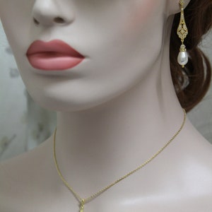 May include: A gold necklace and earrings set with a teardrop-shaped pendant and matching earrings. The pendant and earrings are adorned with clear crystals and a single pearl drop.