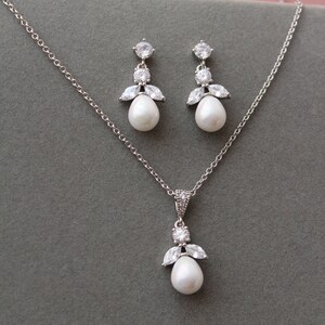 May include: A silver necklace and earrings set with a pearl and crystal accents. The necklace has a delicate chain and a pendant with a pearl drop and crystal accents. The earrings have a pearl drop and crystal accents.