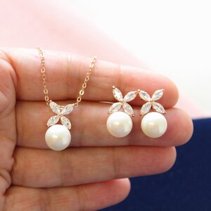 Puede incluir: Un collar y pendientes de oro rosa con un colgante de perla y detalles de flores de cristal.