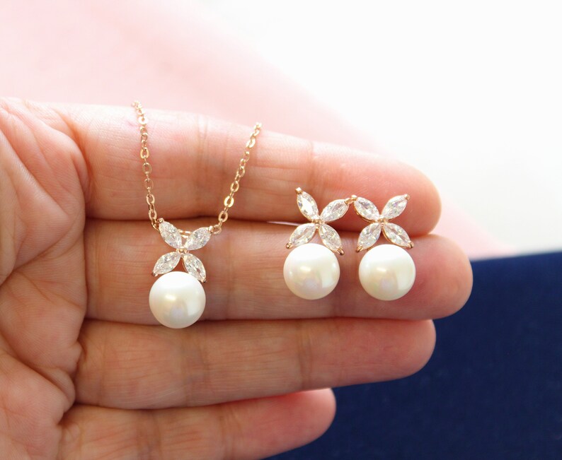 Puede incluir: Un collar y pendientes de oro rosa con un colgante de perla y detalles de flores de cristal.
