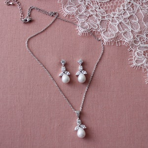 May include: A silver necklace and earrings set with a pearlescent pendant and matching earrings. The pendant and earrings feature a cluster of small clear stones and a larger pearlescent stone.