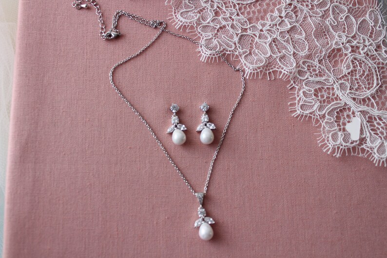 May include: A silver necklace and earrings set with a pearlescent pendant and matching earrings. The pendant and earrings feature a cluster of small clear stones and a larger pearlescent stone.