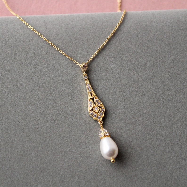 May include: A gold necklace with a delicate, ornate pendant featuring a teardrop shape with clear stones and a single pearl drop.