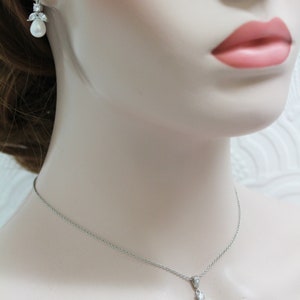 May include: A silver necklace and earrings set with a pearlescent teardrop pendant and matching earrings. The pendant and earrings are accented with small clear cubic zirconia stones.