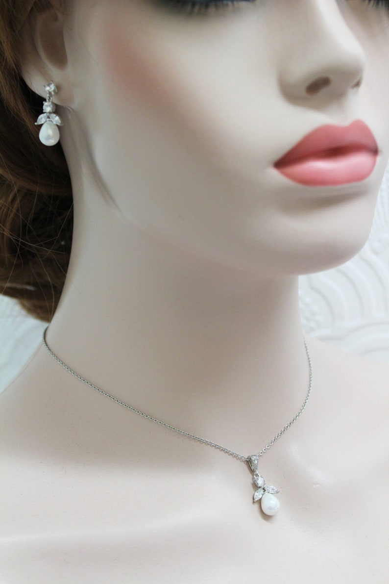 May include: A silver necklace and earrings set with a pearlescent teardrop pendant and matching earrings. The pendant and earrings are accented with small clear cubic zirconia stones.