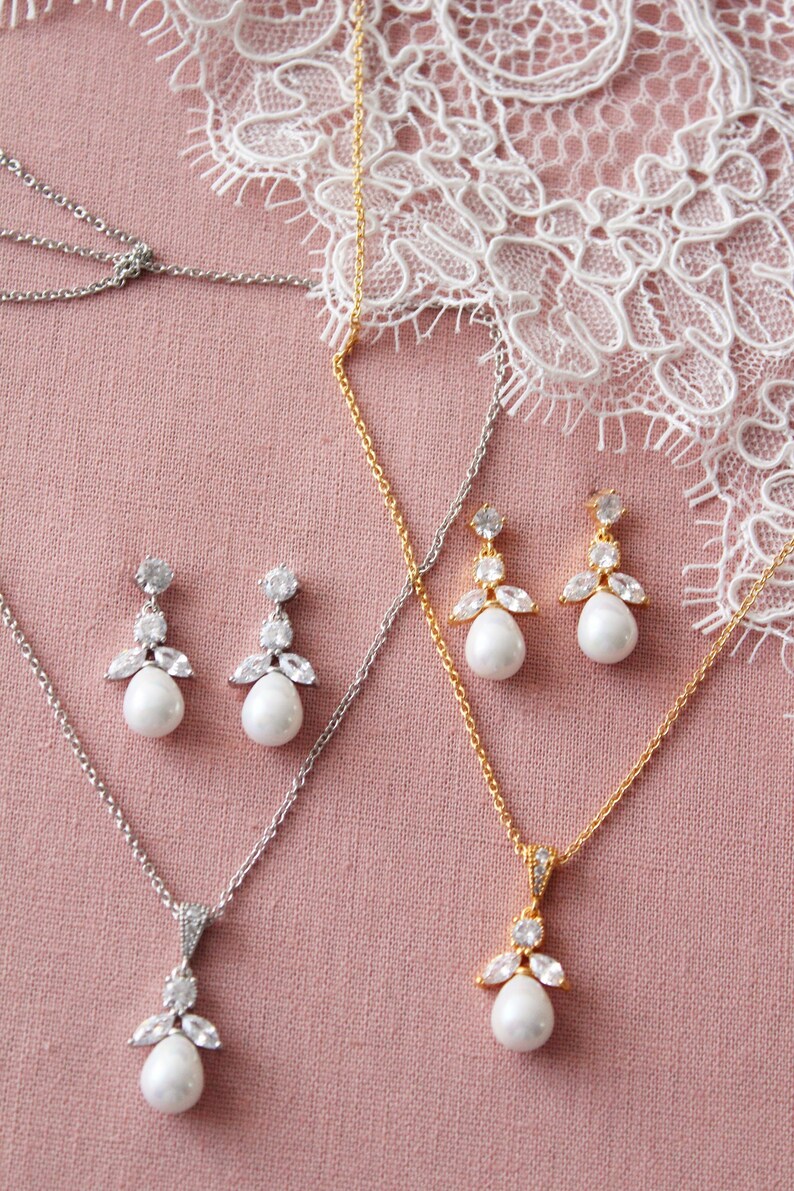 May include: Two sets of bridal jewelry featuring a pearlescent pendant necklace and matching earrings. One set is silver with a silver chain and the other is gold with a gold chain. Both sets feature a pearlescent drop with a crystal cluster.