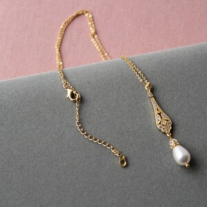 May include: A gold necklace with a delicate pendant featuring a pearlescent drop and a crystal-encrusted design. The necklace has a lobster clasp closure.