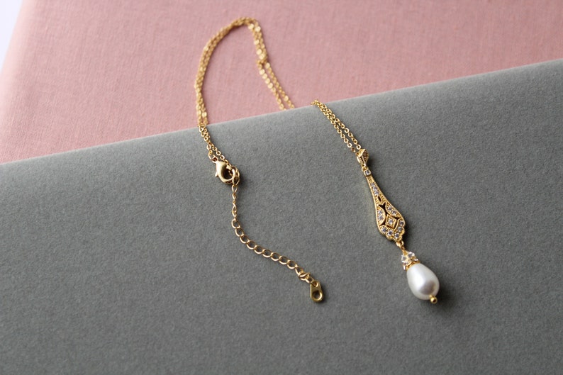 May include: A gold necklace with a delicate pendant featuring a pearlescent drop and a crystal-encrusted design. The necklace has a lobster clasp closure.