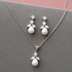 May include: A silver necklace and earrings set with a pearlescent pendant and matching earrings. The pendant and earrings feature a cluster of small clear stones.