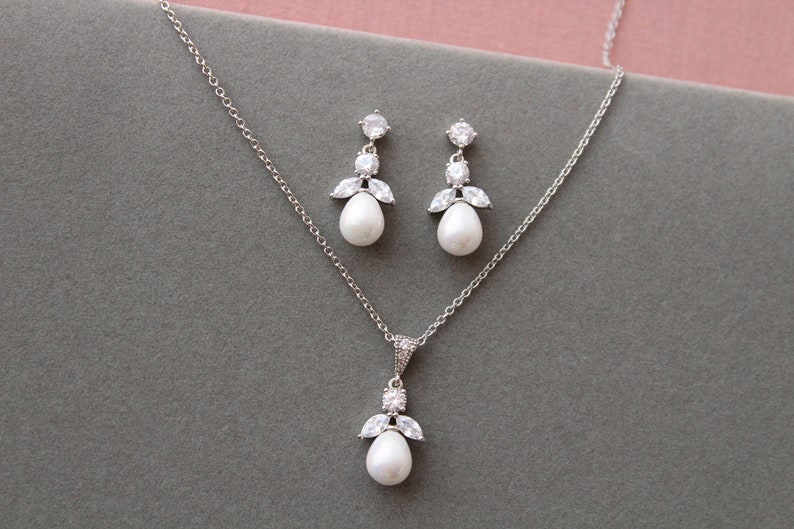 May include: A silver necklace and earrings set with a pearlescent pendant and matching earrings. The pendant and earrings feature a cluster of small clear stones.