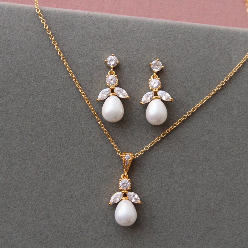 May include: A gold necklace and earrings set with a pearl pendant and crystal accents. The necklace has a delicate chain and the pendant features a pear-shaped pearl surrounded by small crystals.