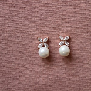 Puede incluir: Un par de pendientes de perla con un peque&ntilde;o dise&ntilde;o de flor hecho de piedras de circonita c&uacute;bica transparentes.
