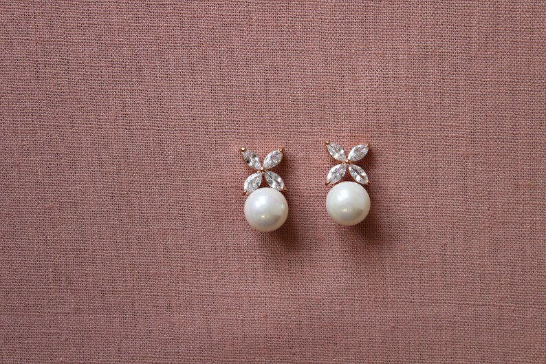 Puede incluir: Un par de pendientes de perla con un peque&ntilde;o dise&ntilde;o de flor hecho de piedras de circonita c&uacute;bica transparentes.