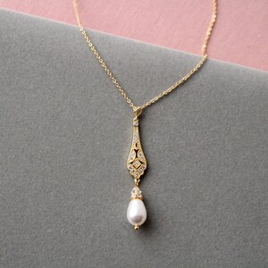 May include: A gold necklace with a delicate pendant featuring a teardrop-shaped design with small clear stones and a single pearl drop.