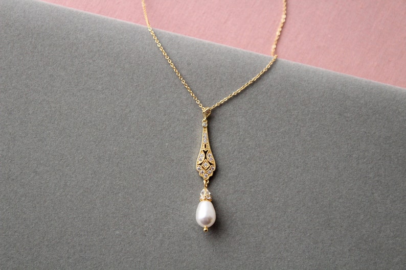 May include: A gold necklace with a delicate pendant featuring a teardrop-shaped design with small clear stones and a single pearl drop.