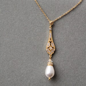 May include: A gold necklace with a delicate pendant featuring a pearlescent drop and a crystal-encrusted design.