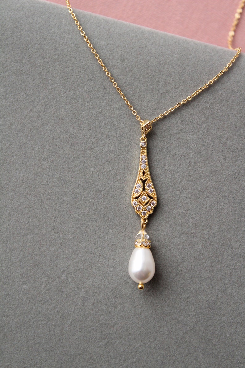 May include: A gold necklace with a delicate pendant featuring a pearlescent drop and a crystal-encrusted design.