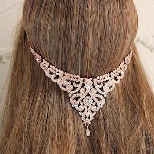 May include: Rose gold hair comb with a delicate, intricate design featuring clear rhinestones. The comb has a teardrop-shaped pendant at the bottom.