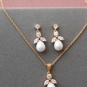 May include: A gold necklace and earrings set with a pearl pendant and matching pearl drop earrings. The pendant and earrings feature a cluster of clear cubic zirconia stones.