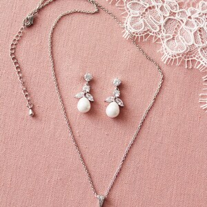 May include: A silver necklace and earrings set with a pearlescent pendant and matching earrings. The pendant and earrings feature a cluster of clear cubic zirconia stones.