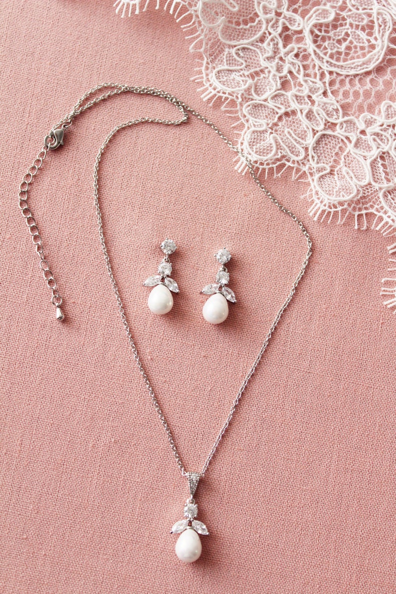 May include: A silver necklace and earrings set with a pearlescent pendant and matching earrings. The pendant and earrings feature a cluster of clear cubic zirconia stones.