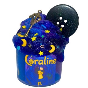May include: A blue container of slime with a galaxy-themed design. The slime is topped with a gold key charm, star and moon-shaped sprinkles, and a large black button. The container has the word "Coraline" and a cartoon illustration.