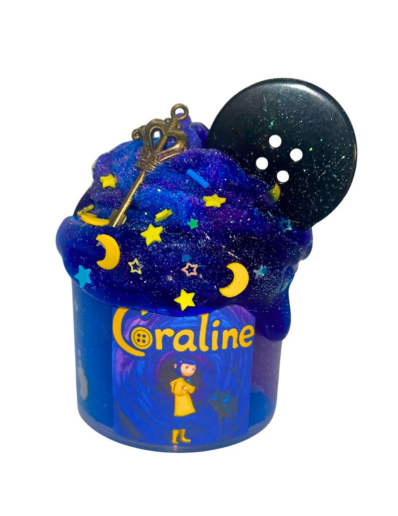 May include: A blue container of slime with a galaxy-themed design. The slime is topped with a gold key charm, star and moon-shaped sprinkles, and a large black button. The container has the word "Coraline" and a cartoon illustration.