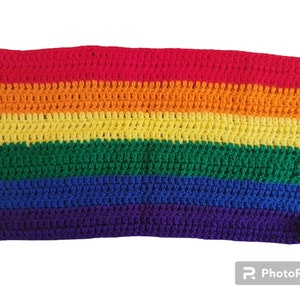 May include: A crocheted item in a rainbow color scheme, featuring horizontal stripes of red, orange, yellow, green, blue, and purple. The handmade textile displays a textured surface and a rectangular shape, suitable for various uses.