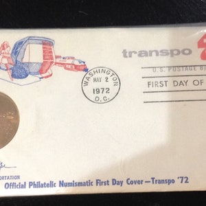 May include: A white envelope with a red and blue illustration of a futuristic vehicle. The envelope has a red "transpo '72" stamp and a circular postmark that reads "WASHINGTON MAY 2 1972 D.C.". The envelope also has the text "U.S. POSTAGE 8¢ FIRST DAY OF ISSUE FIRST U.S. INTERNATIONAL TRANSPORTATION EXPOSITION" and "Official Philatelic Numismatic First Day Cover - Transpo '72".