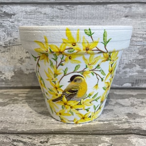 May include: White ceramic flower pot with a yellow bird and yellow flowers painted on it.