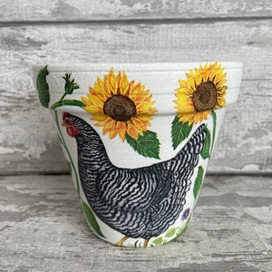 May include: White ceramic flower pot with a black and white chicken and sunflowers painted on it.