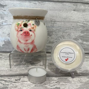May include: White ceramic wax melt burner featuring a pink pig design with floral accents. The burner has a small hole in the top for a tea light. The image also shows a small container of wax melts with the text "Something Different by Linda" and "Made with love".