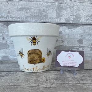 May include: White ceramic flower pot with a bee and honeycomb design. The pot has the text "Save the Bees!" written on it.
