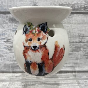 May include: White ceramic wax melt warmer featuring a fox design. The fox is wearing a floral crown and is depicted in shades of red, orange, and brown.