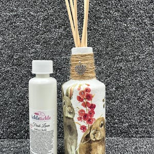 Peut inclure: Une bouteille blanche avec une étiquette qui indique "itchickle home scents" et "Fresh Linen Diffuser Refill". La bouteille est à côté d'une bouteille en verre avec un enveloppement en toile de jute et en ficelle, un charme en forme de cœur argenté et un motif floral avec deux lapins. La bouteille en verre contient des bâtonnets en bois.
