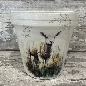 May include: White ceramic planter featuring a watercolour design of a white lamb standing in a field of green grass.