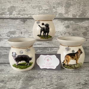 May include: Three ceramic wax melt warmers featuring different dog breeds. The warmers are white with a brown rope trim and a silver heart charm. The dogs are a black Labrador Retriever, a Border Collie, and a German Shepherd.