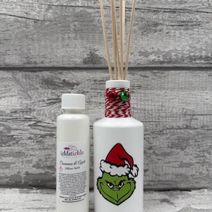 Peut inclure: Un diffuseur blanc avec un motif du Grinch portant un bonnet de Père Noël et une bouteille de recharge de diffuseur Cannelle et Pomme. Le diffuseur a des tiges en bois et est décoré de ficelle rouge et blanche.
