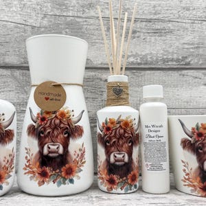 Peut inclure: Ensemble d'accessoires de salle de bain en céramique avec un motif de vache des Highlands. Comprend un distributeur de savon, un vase, un diffuseur, une bouteille et un gobelet. Chaque pièce est blanche avec une tête de vache brune et une couronne florale.