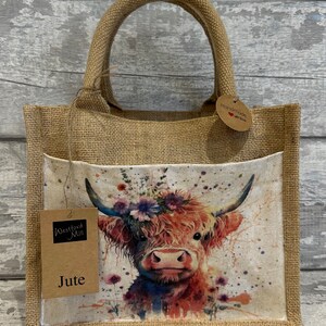K&ouml;nnte beinhalten: Eine braune Jute-Tragetasche mit einem Blumenmuster einer Highland-Kuh. Die Tasche hat eine Tasche auf der Vorderseite mit einem Etikett, auf dem "Westford Mill Jute" steht. Die Tasche hat auch ein Etikett mit der Aufschrift "Handmade with love".