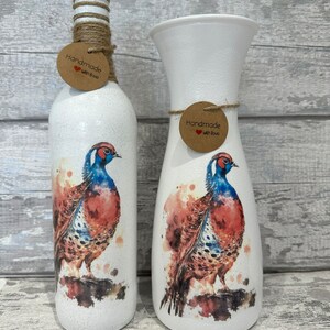 May include: Two white ceramic vases with a watercolor design of a pheasant. The vases are decorated with a brown tag that says "Handmade with Love".