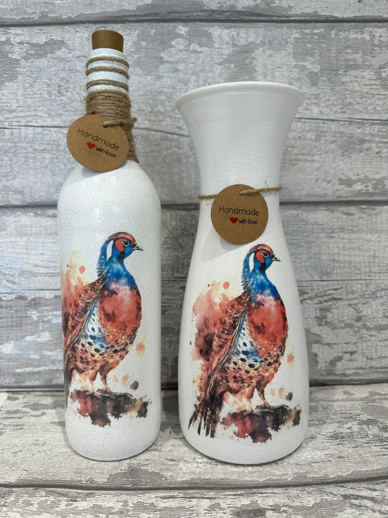 May include: Two white ceramic vases with a watercolor design of a pheasant. The vases are decorated with a brown tag that says "Handmade with Love".